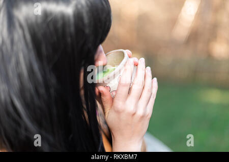 Woman girl black asian hair holding tea cup closeup drinking outside in backyard garden with green matcha herb