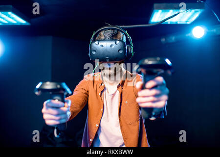 Man playing game using virtual reality headset and gamepads in the dark room of the playing club Stock Photo