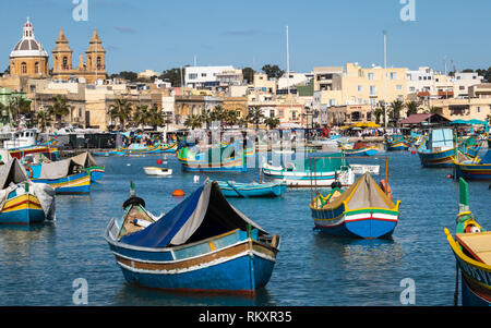 Marsaxlokk Harbour with Traditional, colorful Luzzu Boats in the bay with market in background. Malta, Europe. Stock Photo