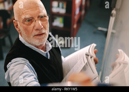Professor in writing on board. Senior man n whiteboard holding a book in hand. Stock Photo