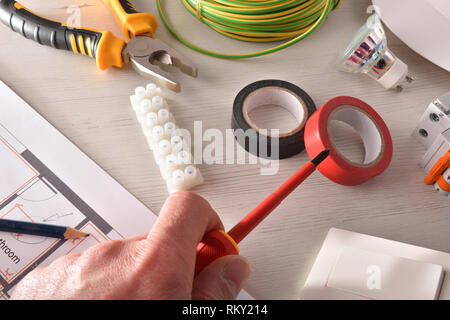 Electrician with screwdriver in his hand on a workbench with tools. Horizontal composition. Front elevated view. Stock Photo