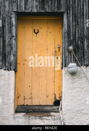 An old yellow wooden door with a horseshoe attached to it, the entrance to a fisherman's hut in Achiltibuie, Ross and Cromarty, Scotland Stock Photo