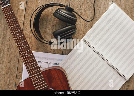Close up view of guitar, professional headphones and musical notes laying on the wooden floor. Musical instruments. Music equipment Stock Photo
