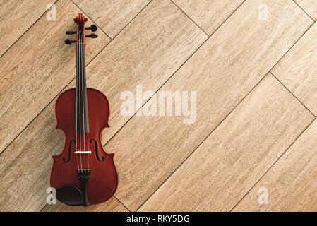 Classic musical instrument. Top view of the brown violin lying on the light wooden floor. Musical instruments. Music equipment. Music background Stock Photo