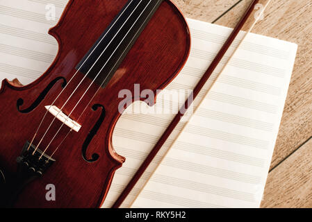 Art of Composing. Close up view of brown violin with a bow lying on sheets for music notes. Violin lessons. Musical instruments. Music equipment. Stock Photo