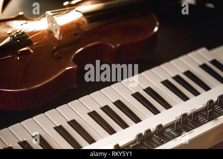 Listening classical music. Close-up view of classical violin instrument lying on a synthesizer. Music concept. Musical instruments. Stock Photo