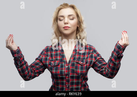 Yoga. Portrait of calm beautiful blonde young woman in casual red checkered shirt standing with crossed arms, smiling, closed eyes, meditating, relaxi Stock Photo