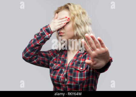 Stop, i dont want to see this. Portrait of beautiful blonde young woman in casual red checkered shirt standing with stop gesture and covering her eyes Stock Photo