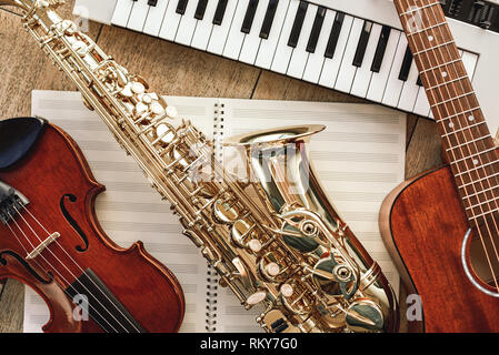Power of music. Top view of musical instruments set: synthesizer, guitar, saxophone and violin lying on the sheets for music notes over wooden floor. Musical instruments. Music equipment Stock Photo