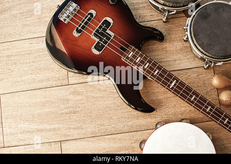 Ready for performance. Top view of musical instruments set: brown electric guitar, drums, gold maracas and tambourine lying on wooden background. Musical instruments. Music equipment. Stock Photo