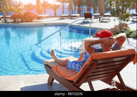 Positive man in red hat resting near the swimming pool hotel in Egypt. Concept beautiful lifestyle Stock Photo