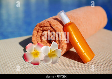 Orange cotton towel and sunscreen body lotion in a orange tube on the background pool. Means for skin care, concept summer of relaxation and sun Stock Photo