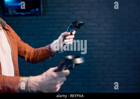 Man playing game using virtual reality gamepads in the dark room of the playing club, close-up view focused on hands Stock Photo