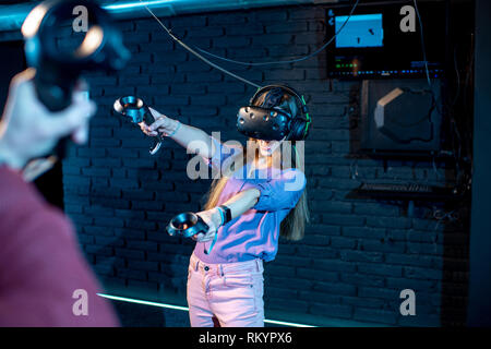 Man and woman playing game using virtual reality headset and gamepads in the dark room of the playing club Stock Photo