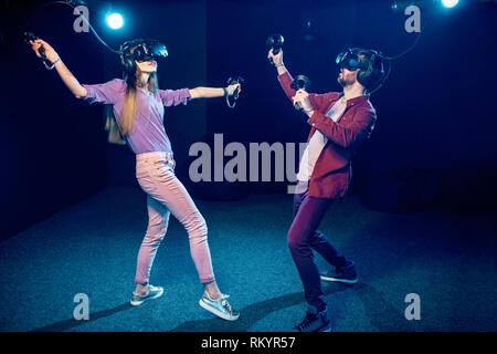Man and woman playing game using virtual reality headset and gamepads in the dark room of the playing club Stock Photo