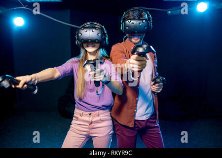 Man and woman playing game using virtual reality headset and gamepads in the dark room of the playing club Stock Photo