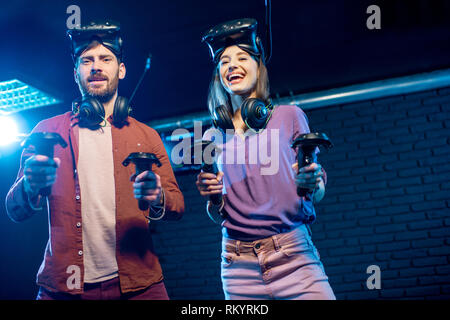 Man and woman playing game using virtual reality headset and gamepads in the dark room of the playing club Stock Photo
