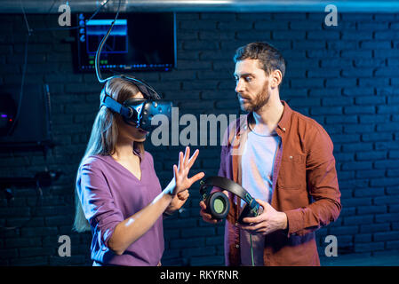 Young woman trying virtual reality with headset standing with man assistant in the playing club Stock Photo