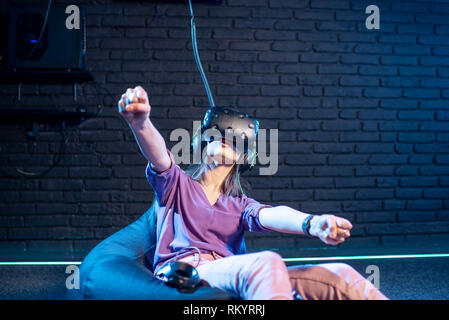 Young woman in virtual reality headset simulating car driving in the dark room of the playing club Stock Photo