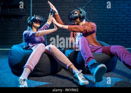 Young couple giving a five each other while playing with virtual reality headsets in the playing club Stock Photo