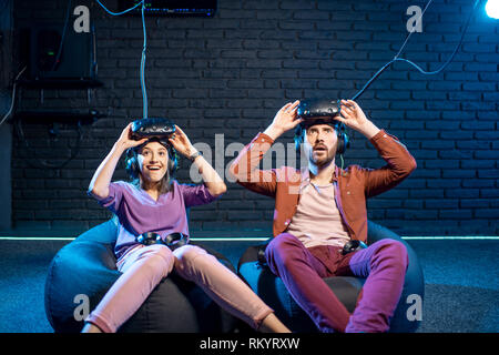 Man and woman with excited emotions sitting together after the game in virtual reality in the playing room Stock Photo