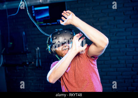 Scared man playing game in virtual reality using VR headset in the playing room Stock Photo