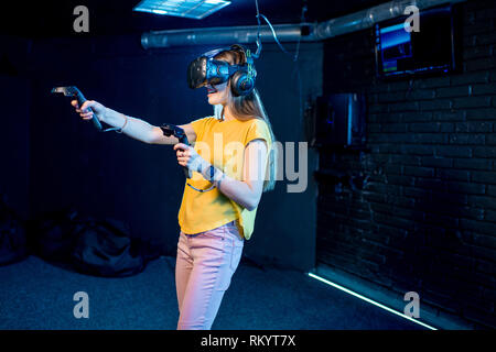 Young woman playing game using virtual reality headset and gamepads in the dark room of the playing club Stock Photo