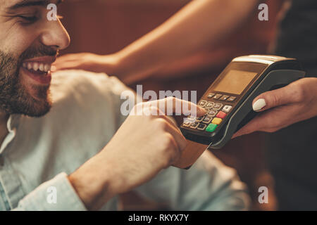 A handsome young man pays to waitress for coffee with credit card in a cafe. Stock Photo