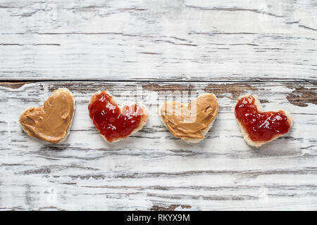 Top view of open face homemade peanut butter and jelly heart shaped sandwiches over a white rustic white wooden table / background. Top view. Stock Photo