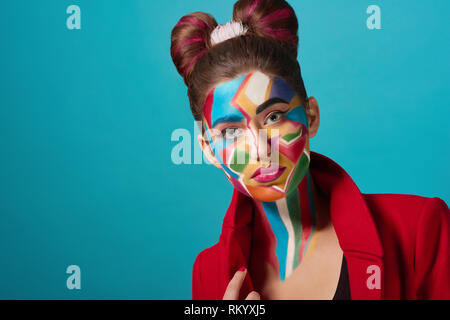 Funky and stylish model wearing in red clothes, has creative, colorful pop art make up. Confident girl has bow hairstyle, looks like comic character. Woman looking at camera. Stock Photo