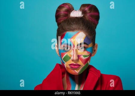 Fashion model looks like comic character, has creative, colorful pop art make up and pink plump lips. Pretty confident woman looking at camera, posing. Stylish bow hairstyle. Stock Photo
