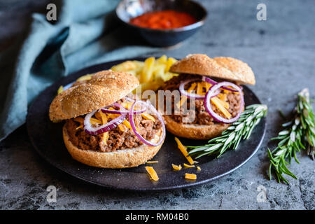 Homemade Sloppy Joe sandwich sprinkled with Cheddar cheese and onion, served with French fries Stock Photo