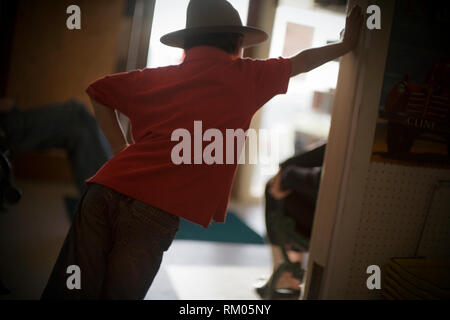 Young boy leaning on a doorframe wearing a hat. Stock Photo