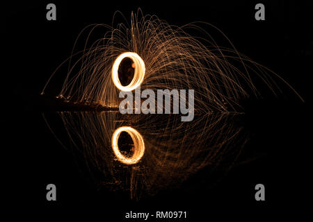 Spark trails at night reflecting off water. Long exposure at night using steel wool. Stock Photo