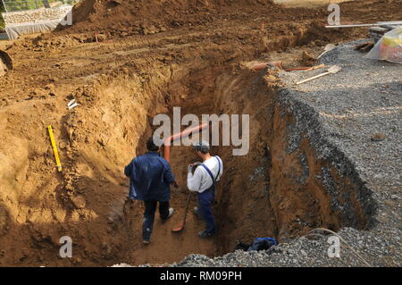 two craftsmen in a construction pit working on a pipe control system Stock Photo