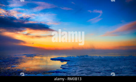 Beautiful  orange and golden colored sunrise clouds and blue sky over frozen lake horizon Stock Photo