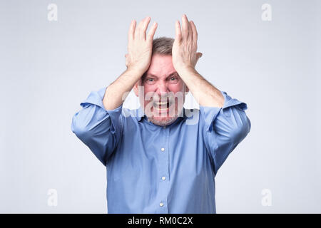 furious senior man holding his head in hands and screaming