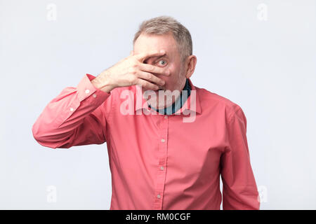 European mature man covering his face by hand and peeping at camera Stock Photo
