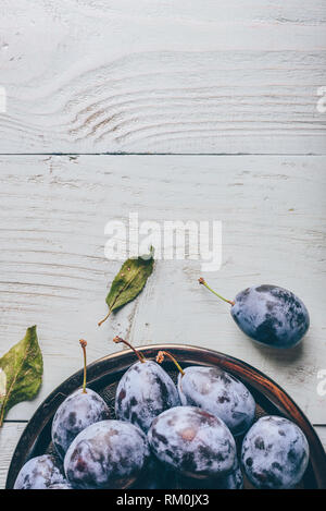 Ripe plums on metal plate over light wooden surface. Copy space Stock Photo
