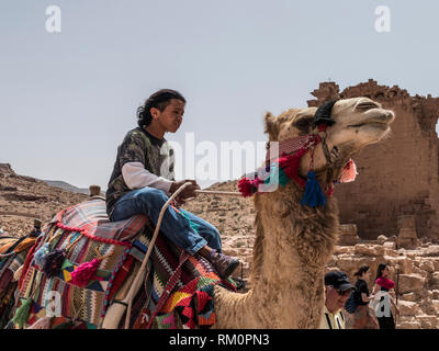 A young Bedouin boy reins in his camel at the base of ruins in Petra in Jordan. Stock Photo