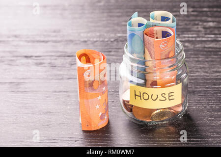 Glass jar with coins and euro notes with the word HOUSE on a black wooden table. The concept of financial savings for the repair, construction of hous Stock Photo
