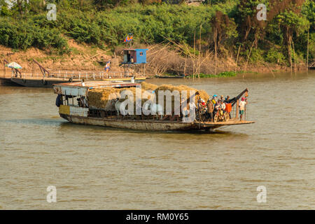 Ferry transports people and  ox pulling traditional wooden carts loaded with hay,  across Mekong River, Cambodia Stock Photo