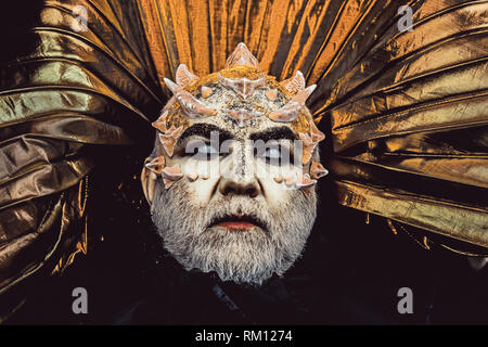 Man with thorns or warts, face covered with glitters. Demon with golden collar on black background. Fantasy concept. Senior man with white beard Stock Photo
