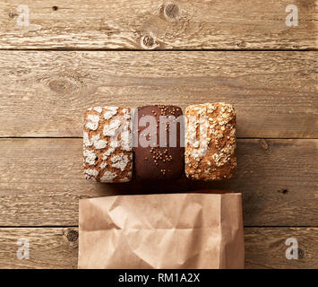 Three loaves of bread on wooden table with paper package. Bakery concept with empty space for design. Gluten-free rye bread with bran and coriander Stock Photo