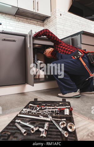 All tools just in case. Seniour handyman repairing washbasin at the kitchen with professional equipment Stock Photo