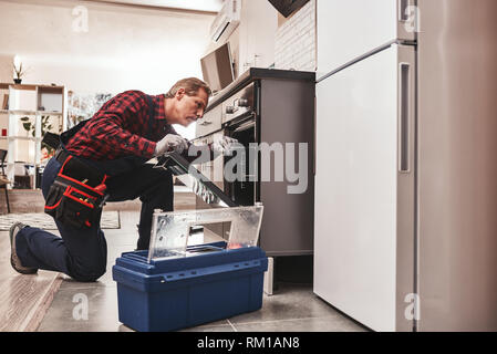 Whats up with oven. Full length of repairman examining oven with flashlight in kitchen with tool case Stock Photo