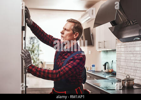Perfect result. Young Male Technician Checking Refrigerator in gloves. Handyman at workplace Stock Photo