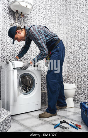 Checking washing machine work. Working man plumber in bathroom testing work of wacher mashine Stock Photo