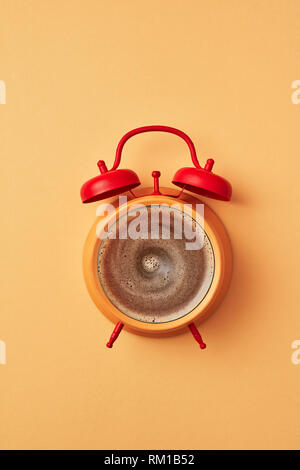 Retro style yellow alarm clock with red bells and fresh coffee instead of dial-plate on an yellow background place for text. Flat lay. Stock Photo