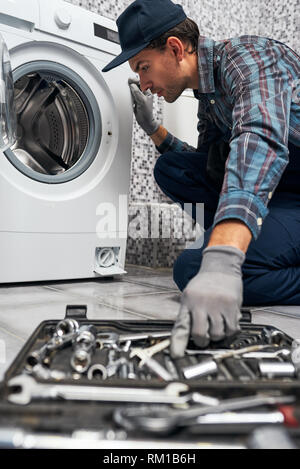 Blurred instruments. Working man plumber in bathroom choose nessesary instrument for repairing washing machine. Stock Photo